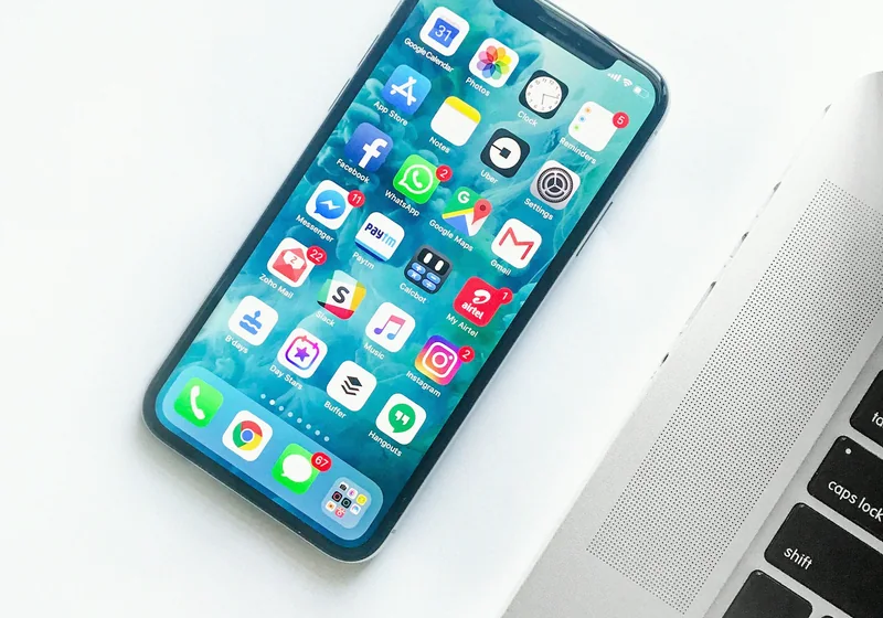 A smartphone full of everyday apps beside a laptop.
